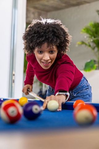 African american woman leaning over blue-felt pool table lining up cue shot showing focused look