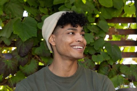 Smiling african american young man wearing beanie on sunlit garden trellis portrait