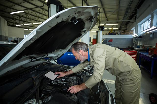 Mechanic using digital tablet while servicing a car engine at repair shop