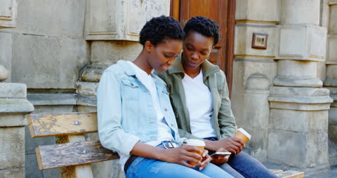 African American Twin Sisters Enjoy Coffee and Mobile Browsing