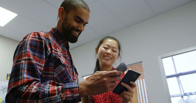 Smiling colleagues discussing work on smartphones in office - Download Free Stock Images Pikwizard.com