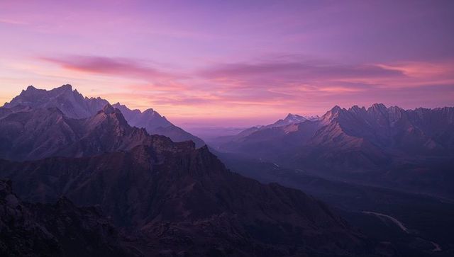 Lavender sunrise over jagged alpine ridge panorama with layered peaks and river valley