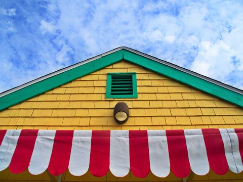 Boasting yellow shingle gable, green trim and red white striped awning under blue sky