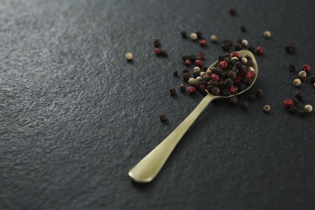 Black pepper and white pepper seeds in a spoon on black background