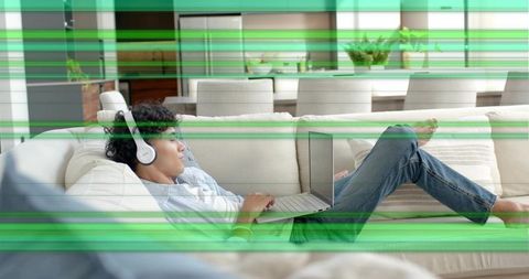 Remote worker reclining on sofa with laptop and headphones in modern open-plan living room