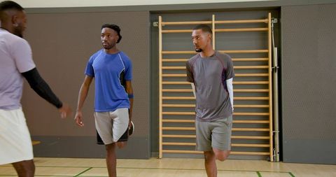 Male athletes practicing single-leg balance drill on indoor basketball court during team training