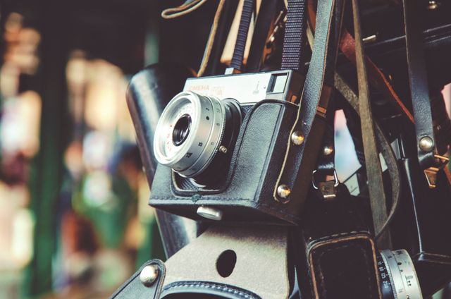 Depicting a vintage film camera hanging on a leather strap, this image captures the essence of nostalgic photography. Ideal for websites or blogs related to photography, antique collections, or retro style themes. It could also be used in designs emphasizing classic technology or vintage aesthetics.