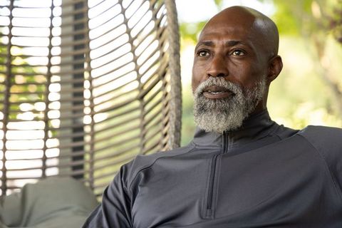 Senior african american man relaxing in wicker chair wearing gray pullover, calm portrait