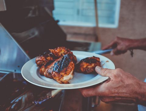 Grilled chicken thighs being plated from outdoor grill