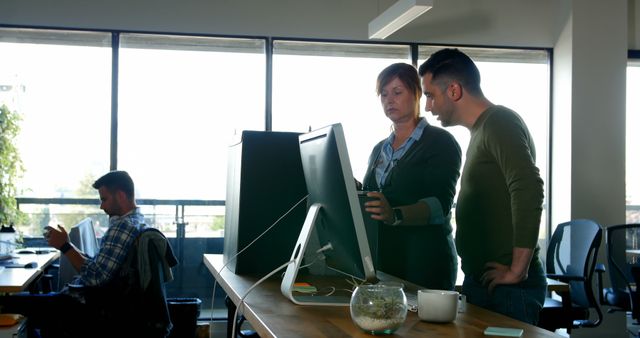 Caucasian male and female colleague using computer at standing desk with colleague in background - Download Free Stock Photos Pikwizard.com