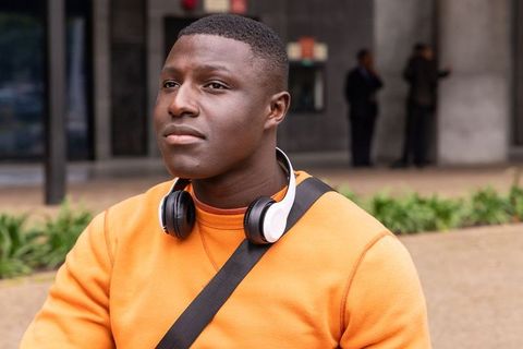 African american man posing with headphones and orange sweater at urban plaza