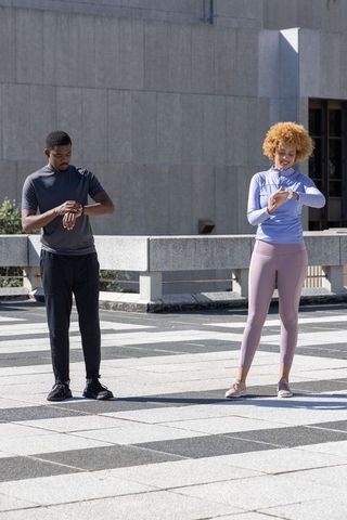Sporty friends checking smartwatches before outdoor urban workout on sunlit rooftop plaza