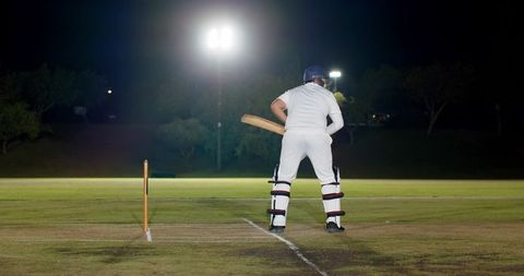 Nighttime cricket batsman standing at crease under floodlights preparing to face delivery