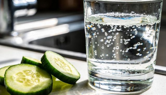 Sparkling water with cucumber slices catching sunlight on kitchen countertop