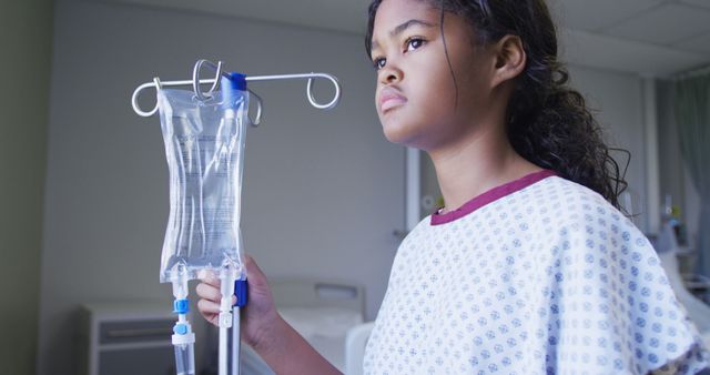 Biracial girl standing with drip bag in hospital room. medicine, health and healthcare services.