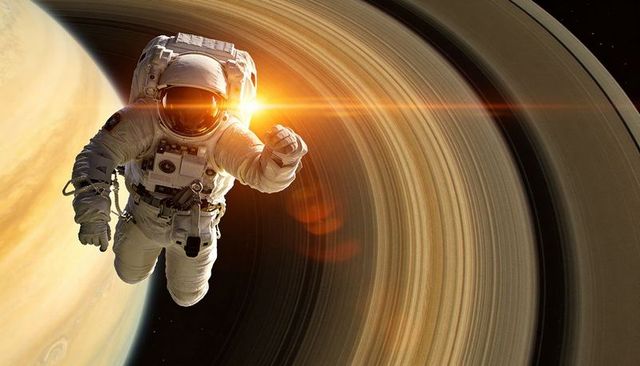 Astronaut floating past ringed gas giant with sun flare reflecting on visor