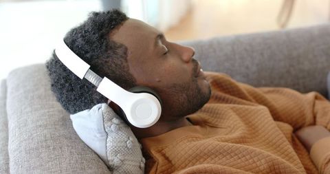 Man relaxing on sofa listening to music with white over-ear headphones at home