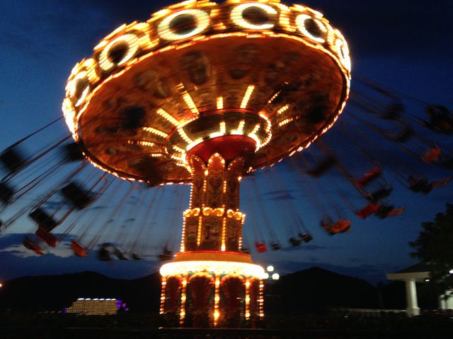 This image captures a brightly lit carousel spinning at night in an amusement park. It can be used for themes of entertainment, fun activities, family outings, carnival experiences, and nocturnal adventures.