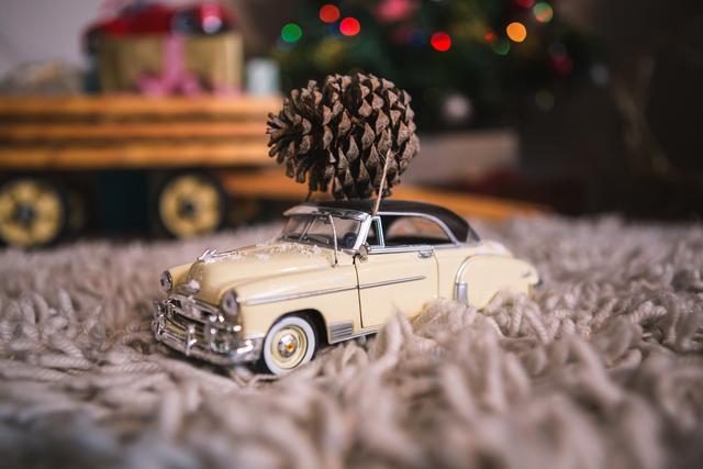 Vintage model car with pine cone on rug during Christmas time. Ideal for holiday-themed promotions, festive greeting cards, nostalgic decor ideas, and Christmas advertisements.