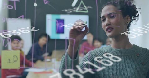 Woman drawing diagrams on glass board during team brainstorming session with sticky notes