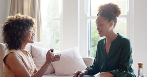 African american woman proposing with engagement ring to partner in sunlit living area