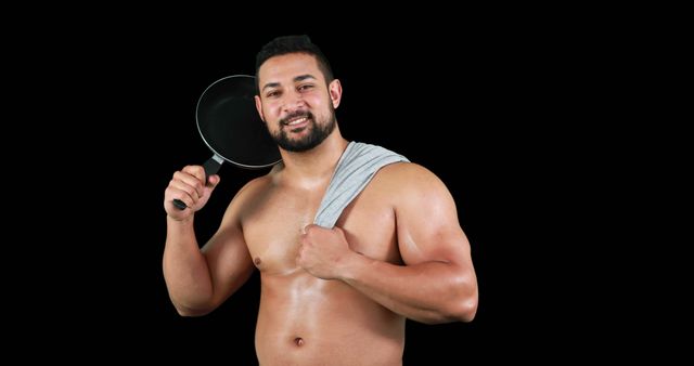 Man with muscular build smiling and holding a frying pan against a black background. Suggesting strength and confidence, suitable for advertisements on fitness, cooking, or kitchenware.