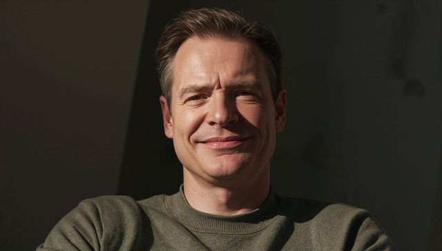 Smiling man wearing olive green sweater posing in dramatic chiaroscuro closeup