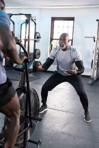 African american trainer coaching client on air bike during intense gym cardio session