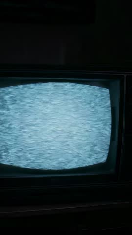 Vertical vintage CRT TV emitting static, hand reaching for dial, moody retro channel change
