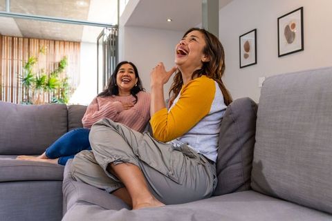 Diverse women laughing together on modern gray sofa at home lifestyle candid friendship