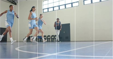 Female Basketball Team Running Drill on Indoor Blue Court with Coach Observing Training