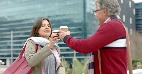 Mature couple toasting with takeaway coffee outside modern glass office building
