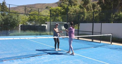 Women shaking hands on blue padel court after friendly match, outdoor club recreation