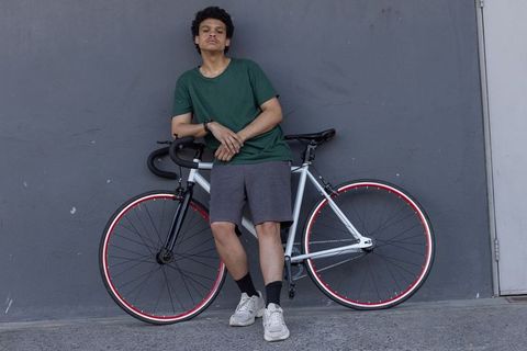 African man leaning on fixed-gear bicycle against urban concrete wall casual commuter