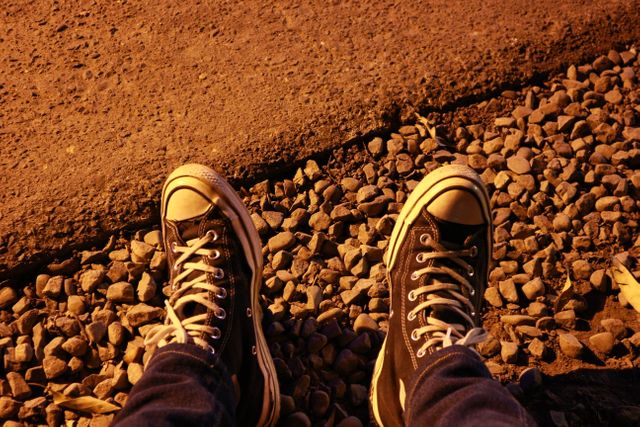 Close-up of casually worn streetwear sneakers on gravel during the night. Ideal for themes of urban life, casual fashion, and night-time street exploration. Can be used in articles about street style, travel blogs, and promotional content for footwear brands or casual apparel.