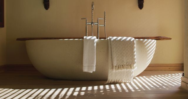 Oval white bathtub in minimal modern bathroom, with lines of sunlight through venetian blind. luxury bathroom interior decor.