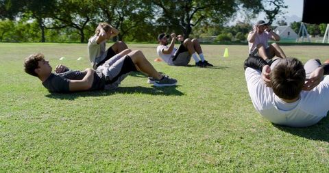 Diverse male group performing crunches on grass field during outdoor fitness bootcamp