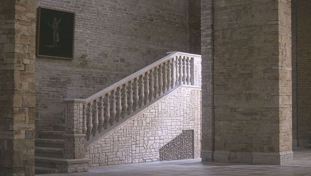 Historic stone staircase rising through sunlit hallway revealing carved balustrade