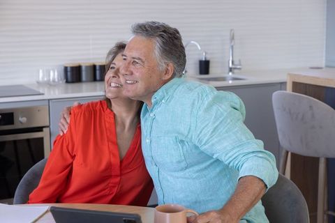 Senior couple embracing in contemporary kitchen using tablet, cozy home lifestyle moment