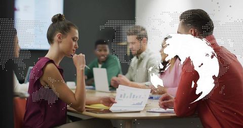 Team reviewing financial charts at round table with global map overlay and laptop collaboration