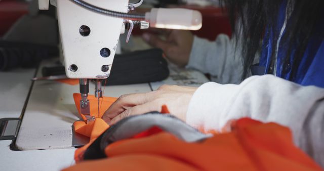 Close-up of a seamstress using a sewing machine, focusing on her hands and the fabric she is working on. Ideal for illustrating topics related to textile and garment production, tailoring, and professionalism in the fashion industry. The image emphasizes craftsmanship and attention to detail, making it suitable for articles, advertisements, or educational materials on fashion design, sewing techniques, and the manufacturing process of clothing.