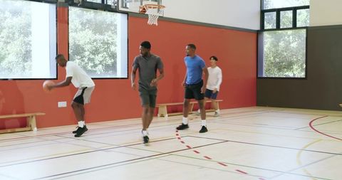 Multiethnic young adults playing pickup basketball indoors, teamwork and athletic training