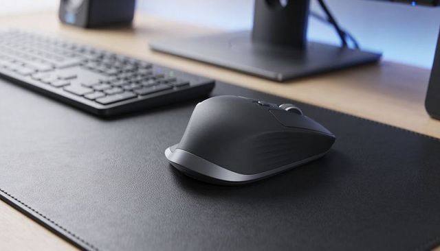 Wireless ergonomic mouse on black leather desk pad with slim keyboard and monitor