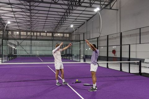 Two male padel players high-fiving at net on vibrant purple indoor court