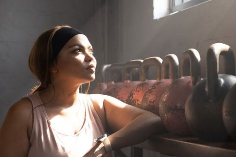 African american woman leaning on kettlebell rack resting in sunlit industrial gym