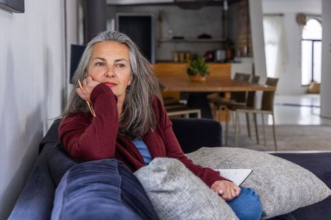 Pensive senior woman journaling on sofa in minimalist living room