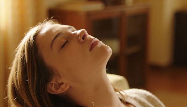 Young woman reclining with closed eyes in cozy golden living room light, serene calm