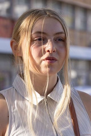 Blonde woman wearing sleeveless zip top with loose hair across face in urban sunlight