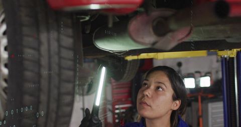 Female mechanic inspecting undercarriage with led work light in auto repair garage