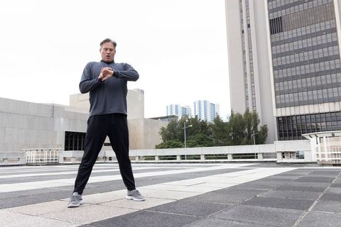 Middle-aged man checking smartwatch on urban rooftop plaza preparing for outdoor run
